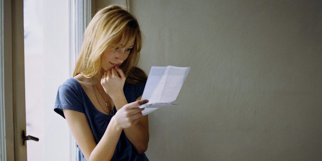 Young woman sitting on window ledge reading letter